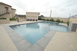 A swimming pool with a stone border, a lounge area with chairs, and a building with a balcony. - Cloud9 Club Resort (A Unit of Dawon Hospitality) (Sasan Gir)