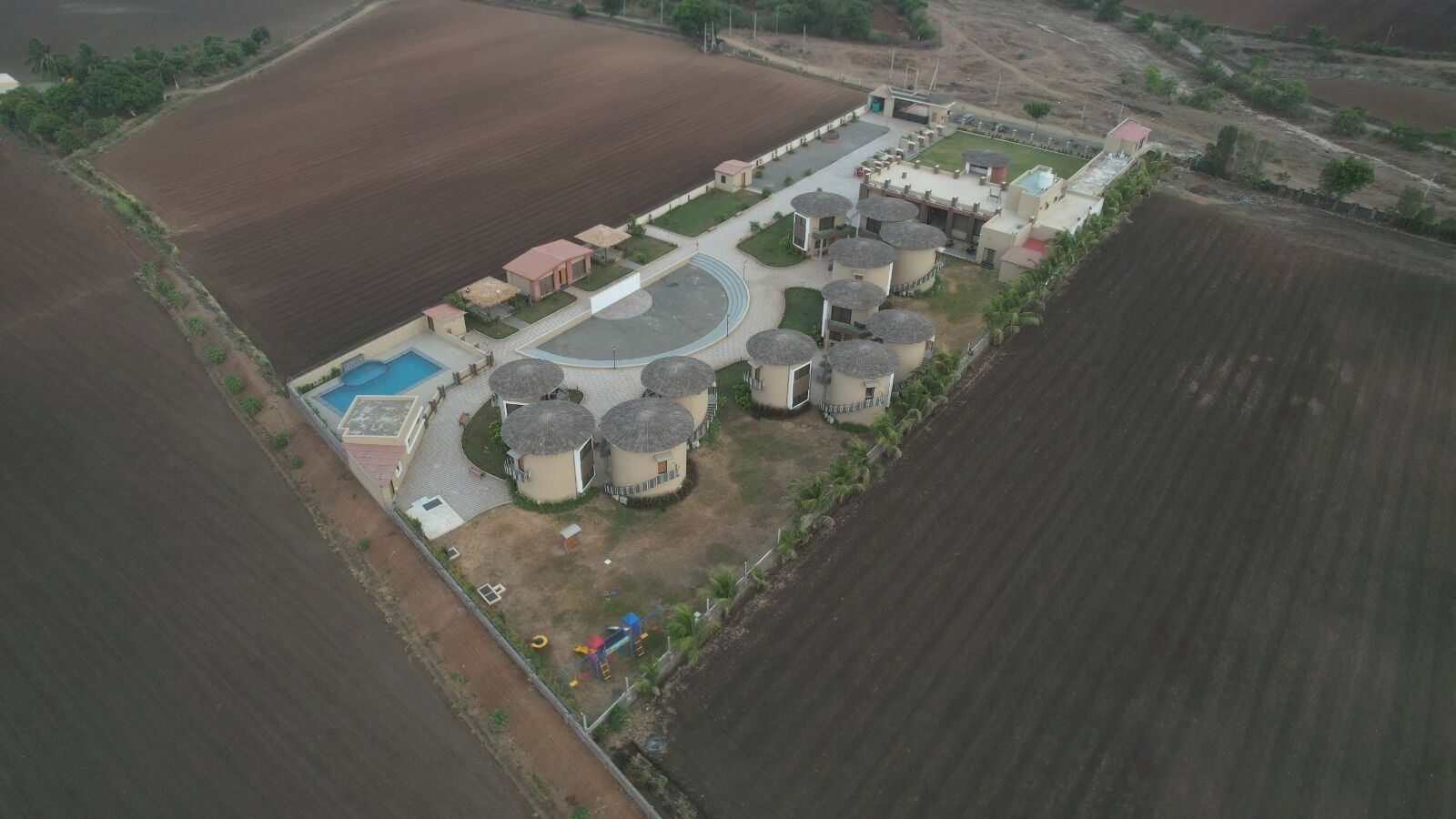 An aerial view of a property with a swimming pool, multiple cylindrical structures, and a landscaped area with a playground.