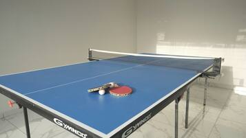 A table tennis table with a net, a red table tennis paddle, and two balls.