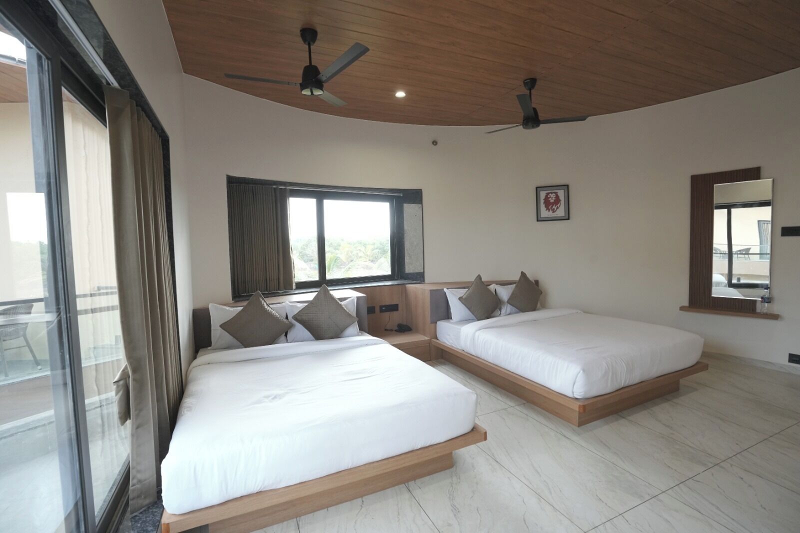 Habitación de hotel con dos camas, ventilador de techo, ventana con cortinas y vistas al balcón.