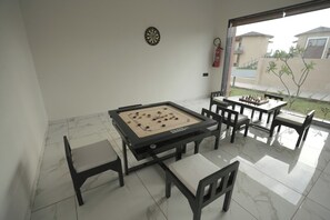 A billiards table with chairs, a dartboard, and a fire extinguisher in a room with a view of the outside.