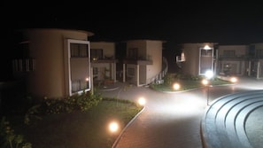 Een nachtzicht van een hotel met meerdere gebouwen, verlichte paden en kleine tuinen.