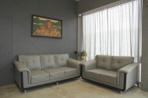 A room with two beige sofas, a framed painting of lions, a potted plant, and a window with sheer curtains.