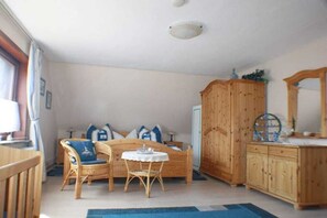 A room with a bed, a wooden wardrobe, a wicker chair, a small table, and a mirror. - "At Hahnheide" || Linau (Linau)