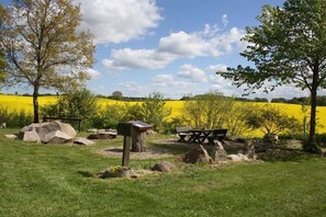 A picnic area with a bench, a stone table, and a plaque, surrounded by grass and trees. - "At Hahnheide" || Linau (Linau)