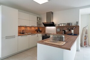 A modern kitchen with white cabinetry, a wooden countertop, and a central island. - Holiday home with 2 bedrooms (18445 Kramerhof, Deutschland)