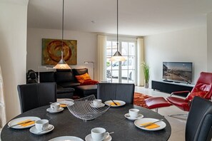 A modern living room with a round dining table set for four, a black sofa, a red armchair, and a television on a black stand. - Holiday home with 2 bedrooms (18445 Kramerhof, Deutschland)