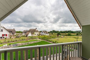 A view from a balcony overlooking a residential area with houses, a well-maintained lawn, and a stone wall. - Holiday home with 2 bedrooms (18445 Kramerhof, Deutschland)