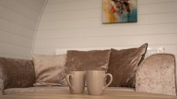 A room with a wooden table, two beige mugs, a beige sofa, and a painting of a bird on the wall.