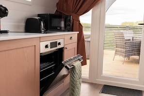 A kitchen with a microwave, oven, and a view of the outdoors through a glass door. - Pepperwood Pods (Spilsby)