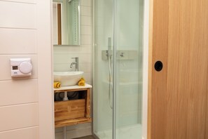 Un bany modern amb plat de dutxa de vidre, un lavabo blanc i un moble de bany de fusta.