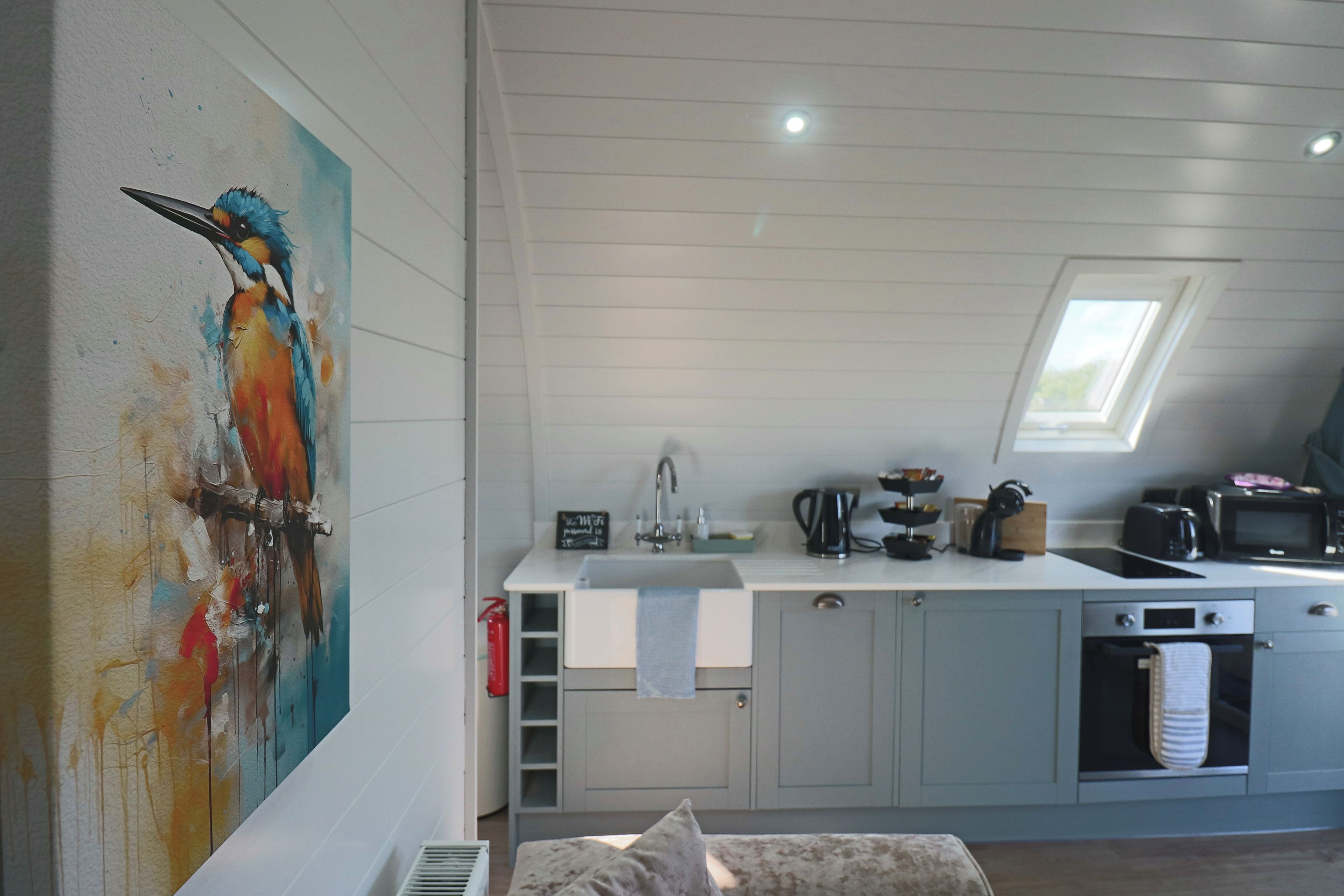 A modern kitchen with a skylight, a painting, and a cat on a bench.
