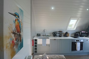 A modern kitchen with a skylight, a painting, and a cat on a bench. - Pepperwood Pods (Spilsby)