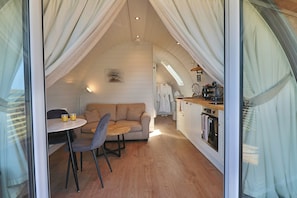 A cozy, compact living space with a kitchenette, a dining area with a table and chairs, and a sofa. - Pepperwood Pods (Spilsby)