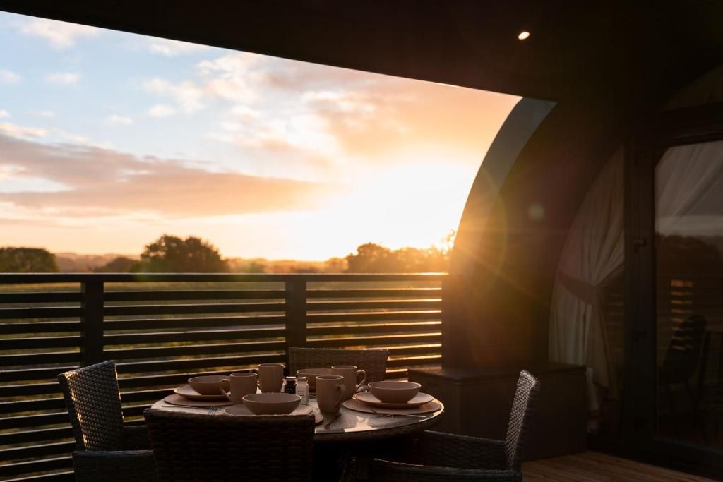 A dining table with chairs and bowls on a balcony overlooking a sunset.