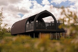 Un edifici modern amb teulada corbada i teulada plana, situat en un camp verd amb un cel clar i núvols al fons.