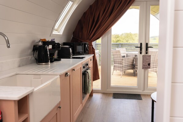 Una kitchenette con un lavamanos, cafetera, microondas y tostadora. Hay una puerta corrediza que da a un espacio exterior con una mesa y sillas.