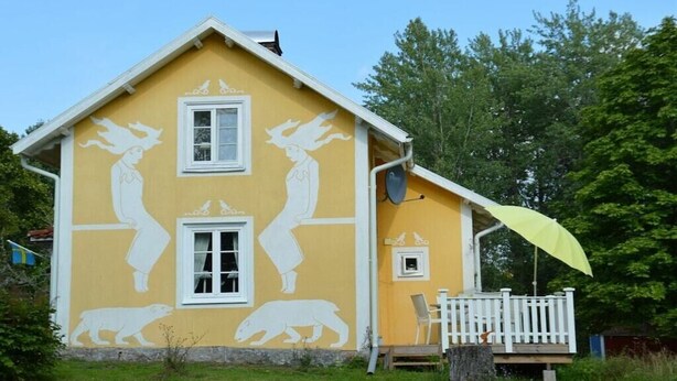 Une maison jaune avec des encadrements de fenêtres blancs et un porche blanc.