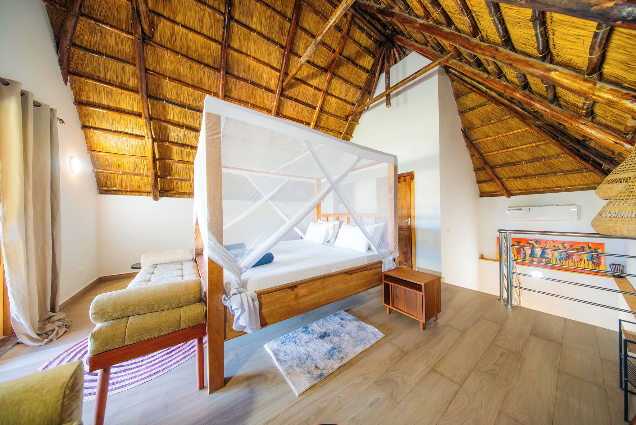 Une pièce avec un lit, une petite table, une chaise, un plancher en bois et un toit de chaume.