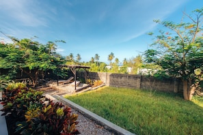 A garden with a pergola, seating area, and a stone wall. - Beachside Villa - Pool, WiFi, AC & Kitchen (Pwani Mchangani)