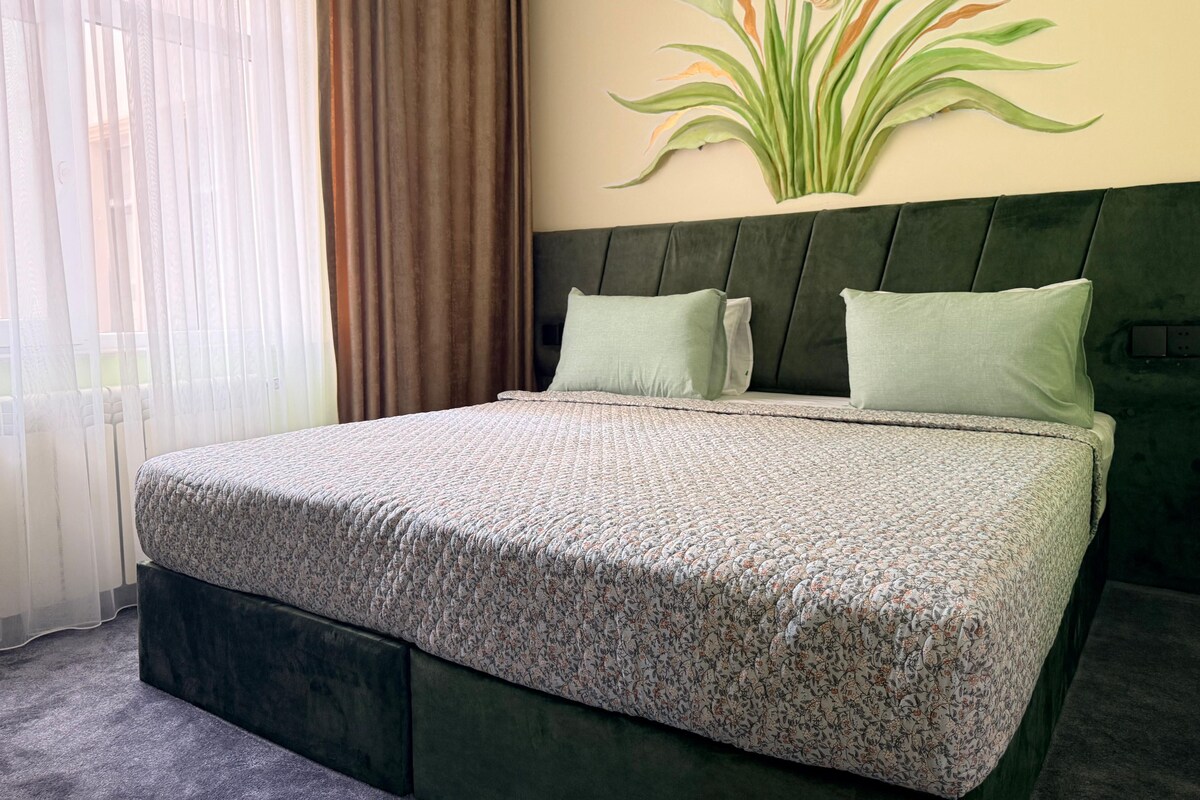 A bed with a floral bedspread, two pillows, and a headboard with a plant mural.