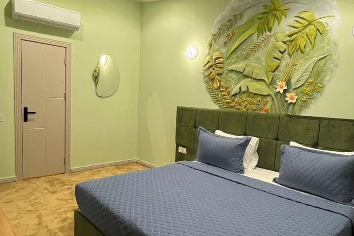 A bedroom with a bed, a wooden desk, a wall-mounted air conditioner, and a door.