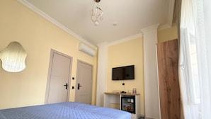 Un dormitorio con cama, televisor, refrigerador pequeño y puerta de madera.