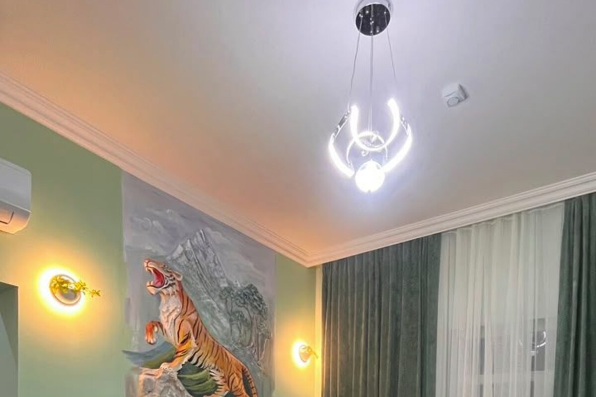 A hotel room with two beds, a tiger mural, and a ceiling light fixture.