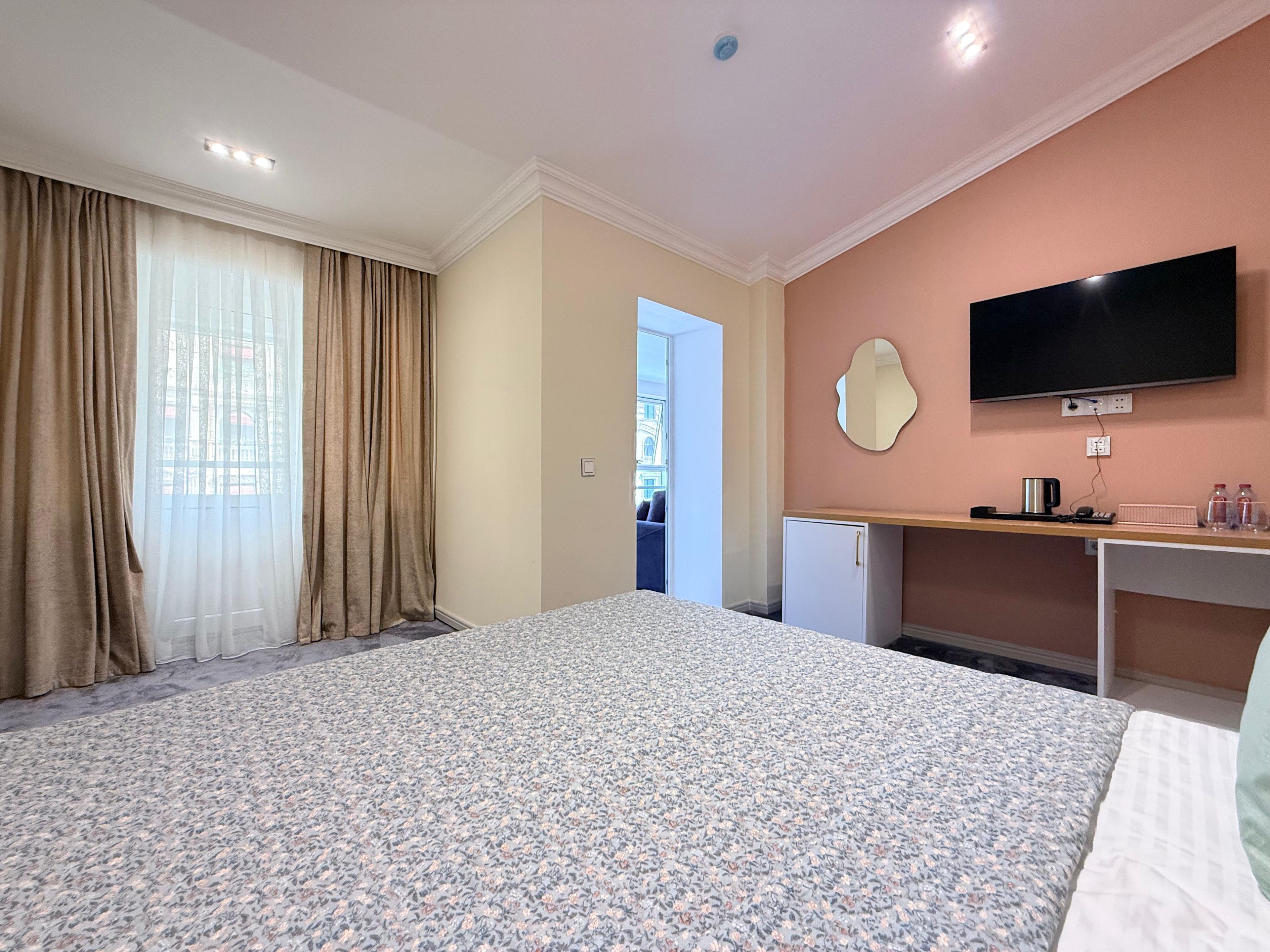 A hotel room with a bed, a desk, a television, and a view of the outside.