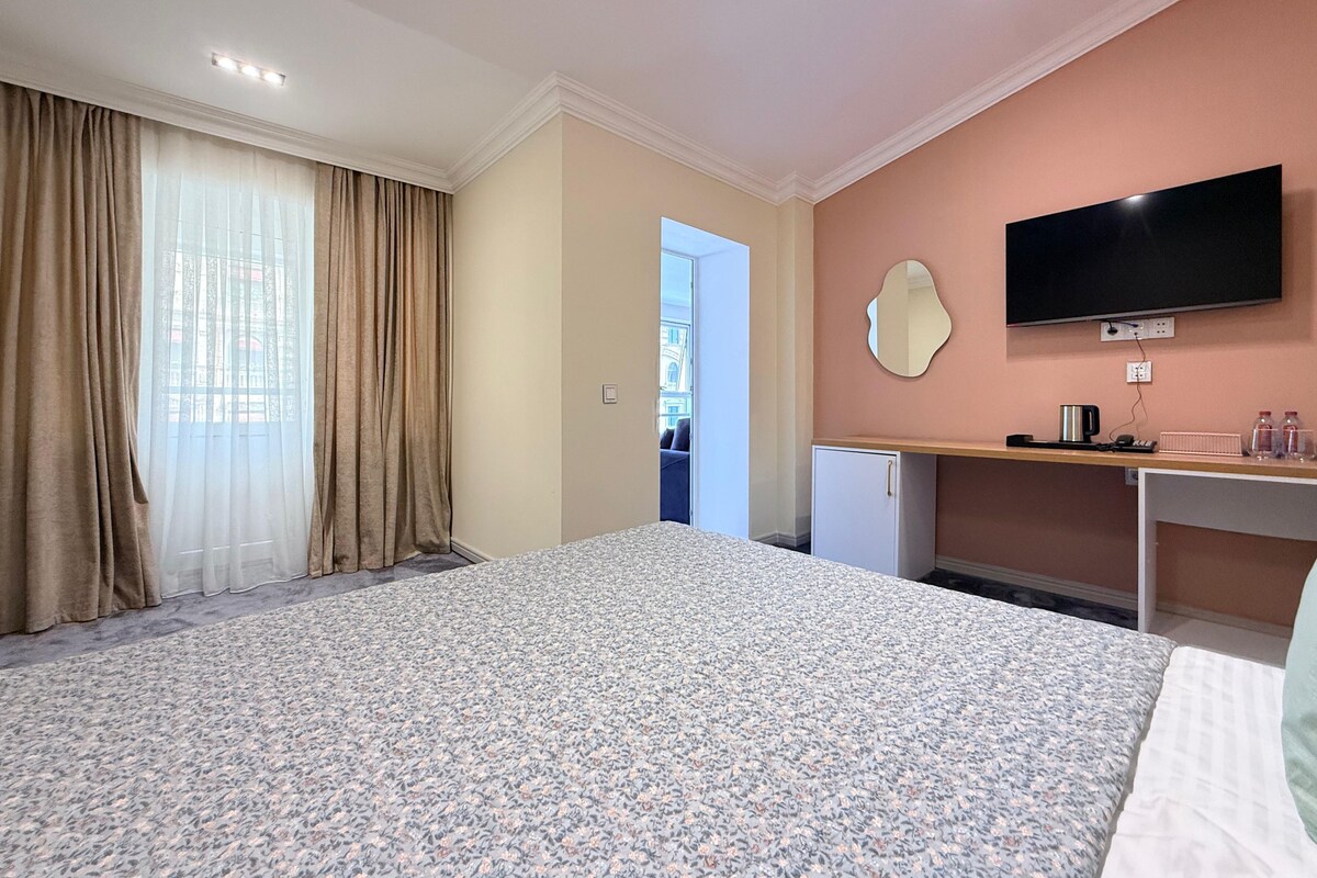 A hotel room with a bed, a desk, a television, and a view of the outside.