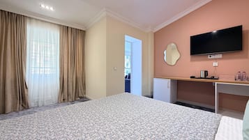 A hotel room with a bed, a desk, a television, and a view of the outside.