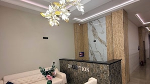 Un área de recepción con pared de mármol, un mostrador de recepción, un sofá y una mesa de centro.