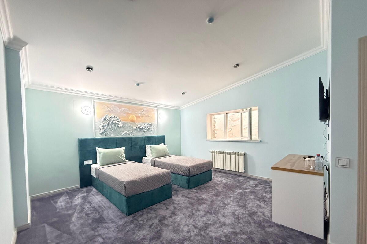 A bedroom with two beds, a radiator, a TV, and a painting on the wall.
