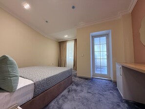 A bedroom with a bed, a desk, a door, and a window with curtains.