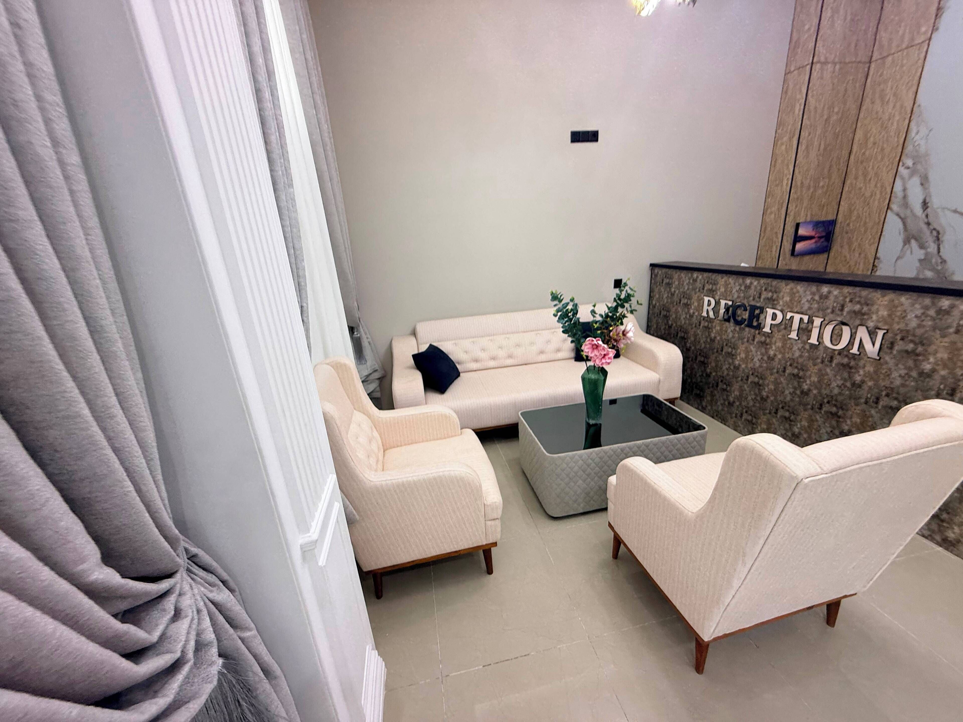 Un área de recepción con un sofá, sillones, una mesa de centro y un mostrador de recepción.