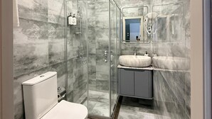 Un baño moderno con ducha envuelta en vidrio, un inodoro y un tocador con espejo.