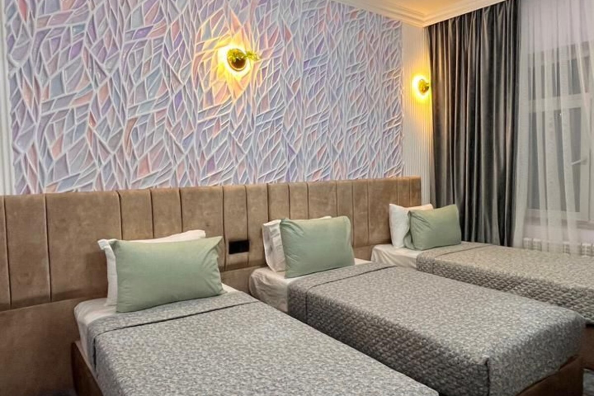 A hotel room with two beds, a patterned wall, a ceiling light, and a window with curtains.