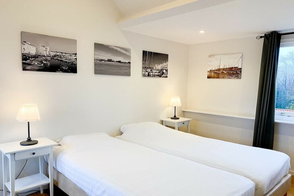 A hotel room with two beds, a nightstand with a lamp, and three black-and-white photographs on the wall.