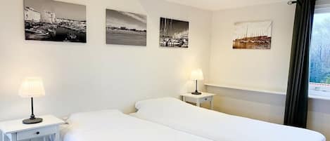 Una habitación de hotel con dos camas, una mesita de noche con lámpara y tres fotografías blanco y negro en la pared.