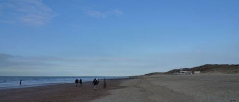 Una playa con cielo despejado, algunas personas caminando y una estructura a la derecha.
