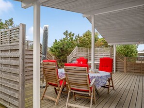 An outdoor patio with wooden deck, two wooden chairs with red cushions, a small round table with a floral tablecloth, and a covered area with a wooden railing. - "Jale" - 300m from the sea by Interhome (Thisted)
