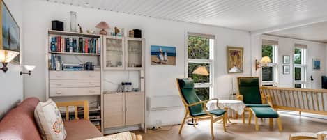 A well-lit room with a sofa, chairs, a bookshelf, and a dining area.