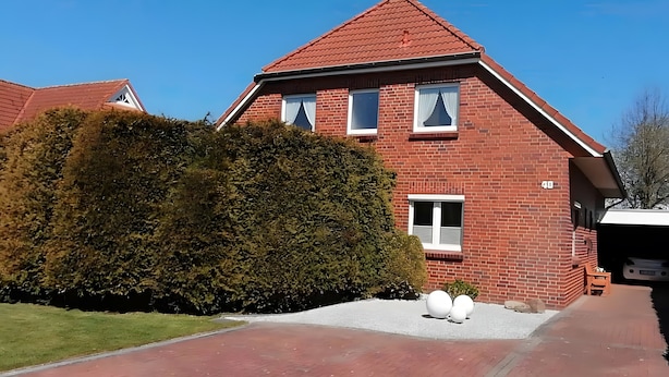 Ein rotbackenförmiges Haus mit einem geneigten Dach, einem gepflegten Rasen und einer Auffahrt zum Eingang.