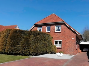 A red-brick house with a sloped roof, a well-maintained lawn, and a driveway leading to the entrance.