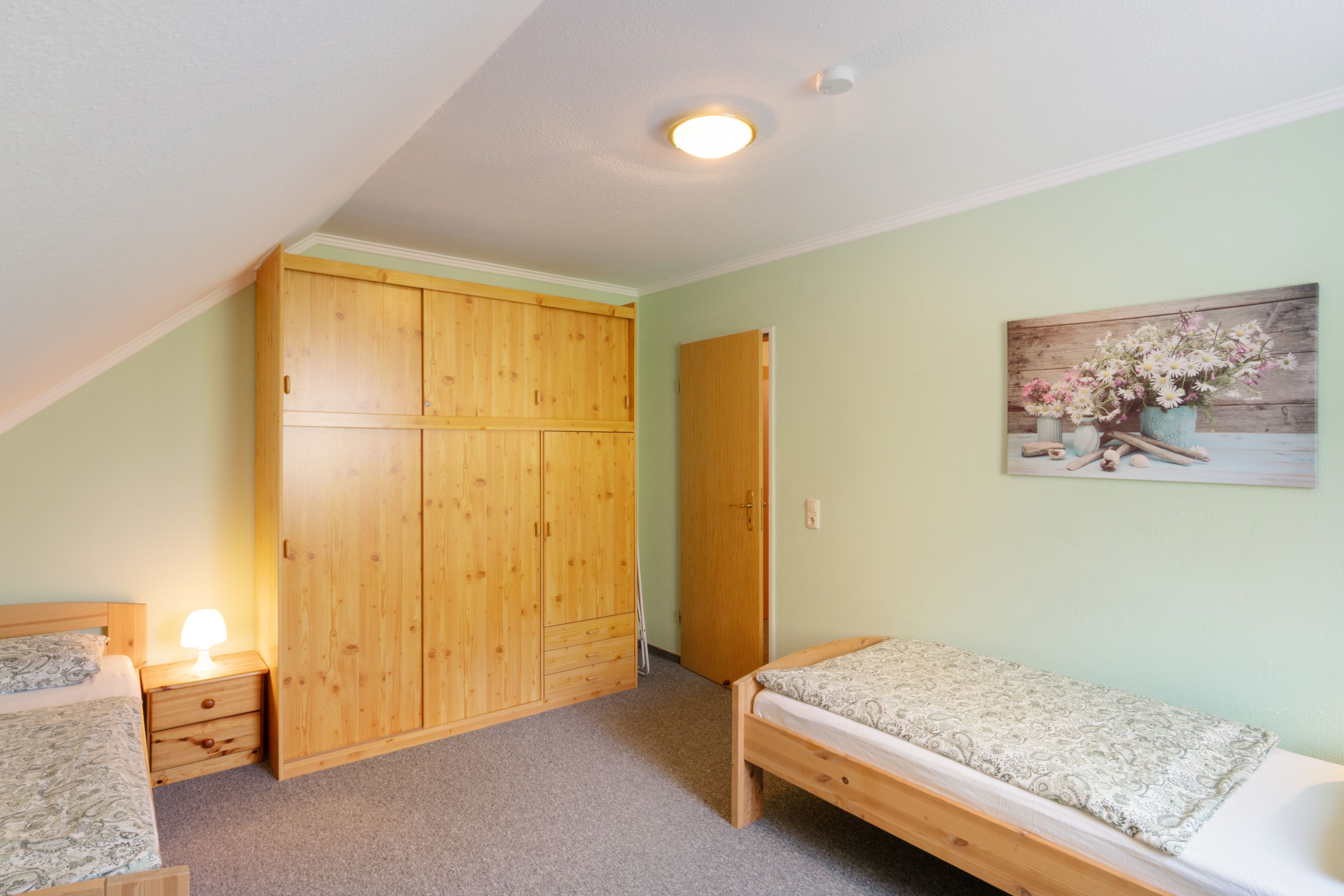 Un dormitorio con un armario de madera, una cama individual, una mesita de noche y una lámpara de pared.