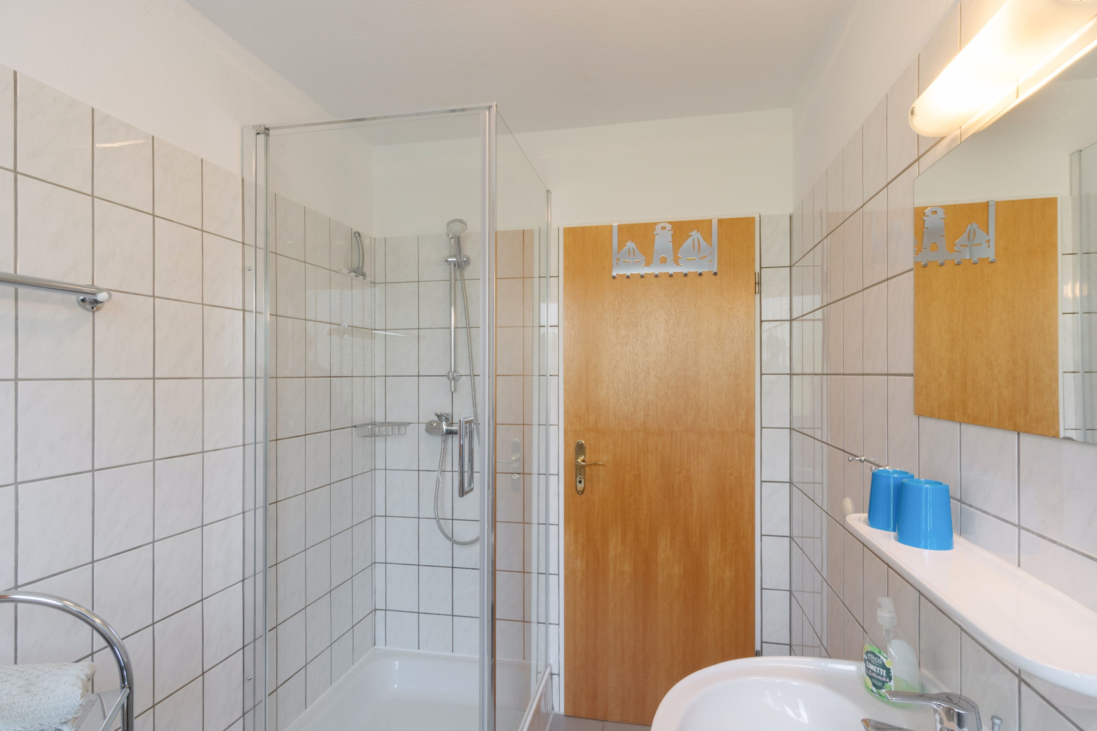 A modern bathroom with a glass-enclosed shower, a wooden door, and a white sink with a mirror above it.