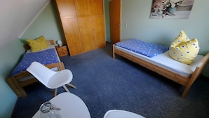 Ein kleines, gemütliches Zimmer mit einem Bett, einem Sessel, einem Tisch und einem Kleiderschrank.