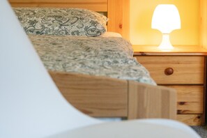 Una cama con una colcha y almohadas estampadas, una mesita de noche con una lámpara y una mesita auxiliar de madera.
