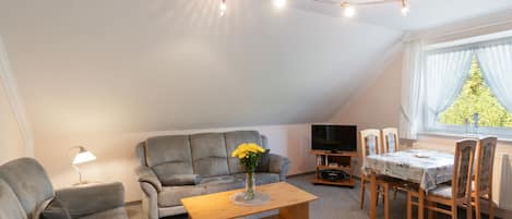 A cozy living room with a sofa, a coffee table, a TV, and a dining area with chairs and a table.