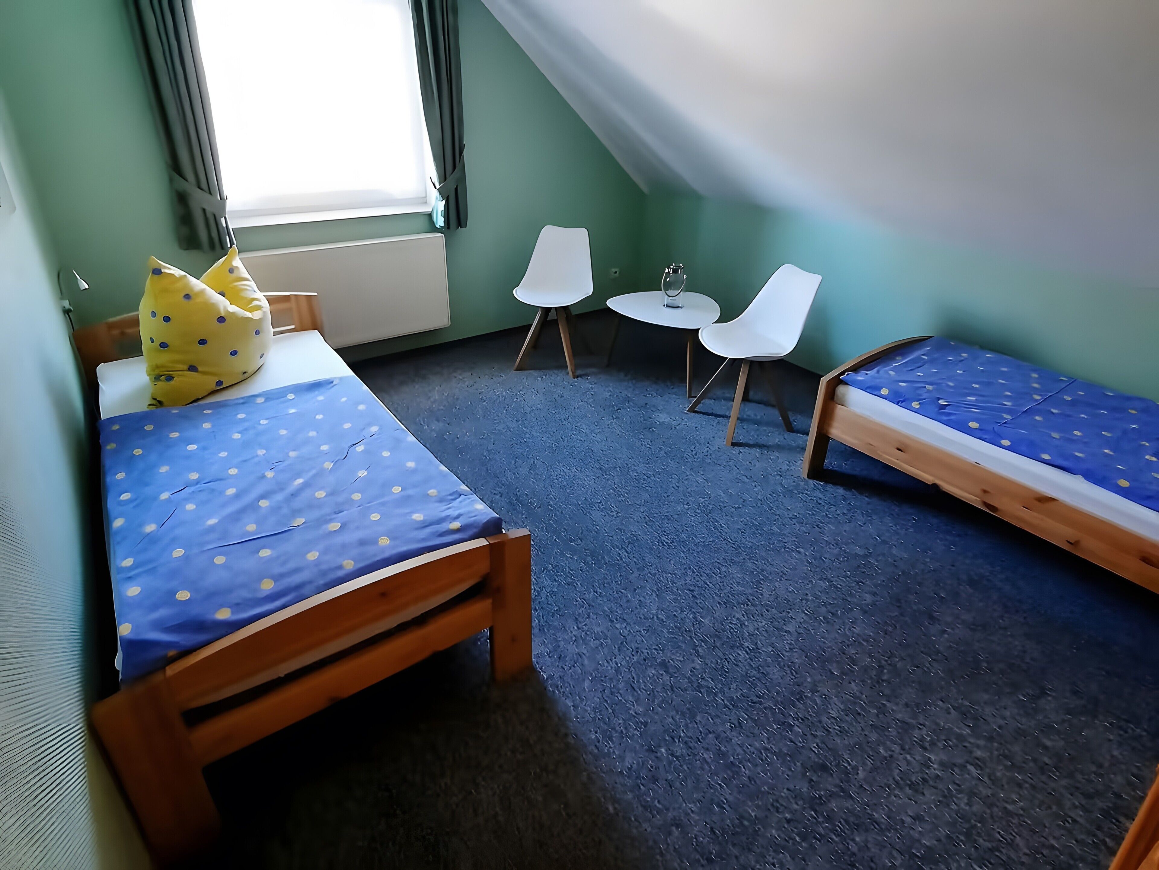 Une chambre avec deux lits, une petite table, deux chaises et une fenêtre avec des rideaux.